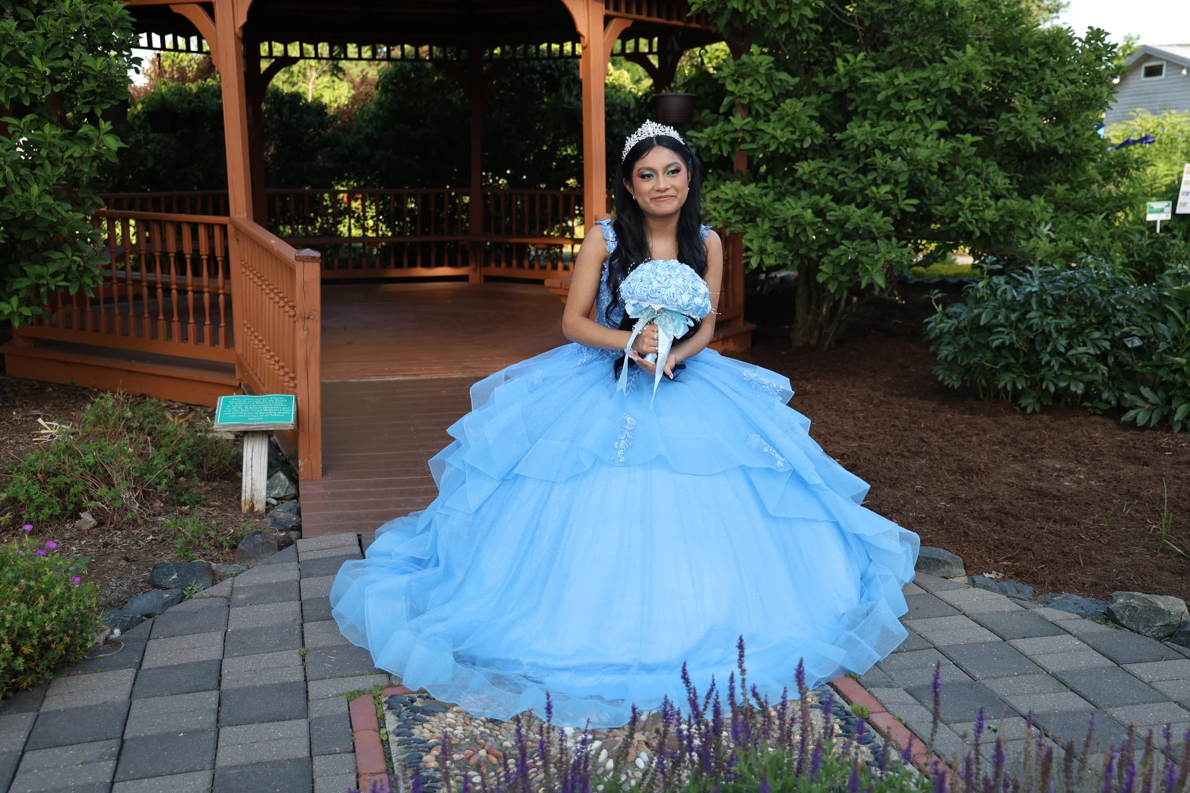 Quinceañera in her full blue dress among flowers and greenery
