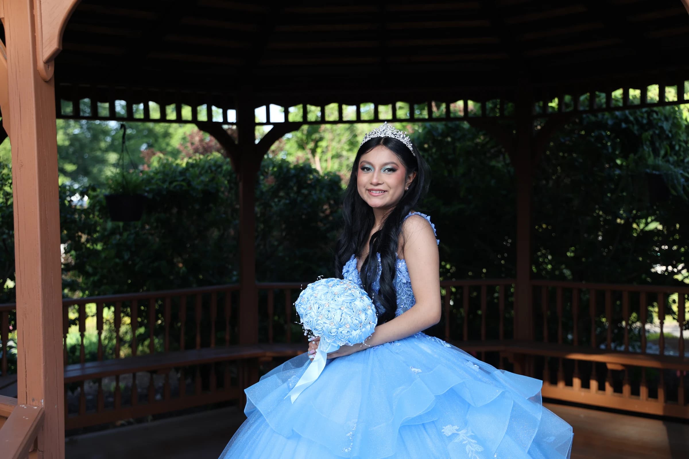 Quinceañera portrait in a blue gown beneath a wooden gazebo