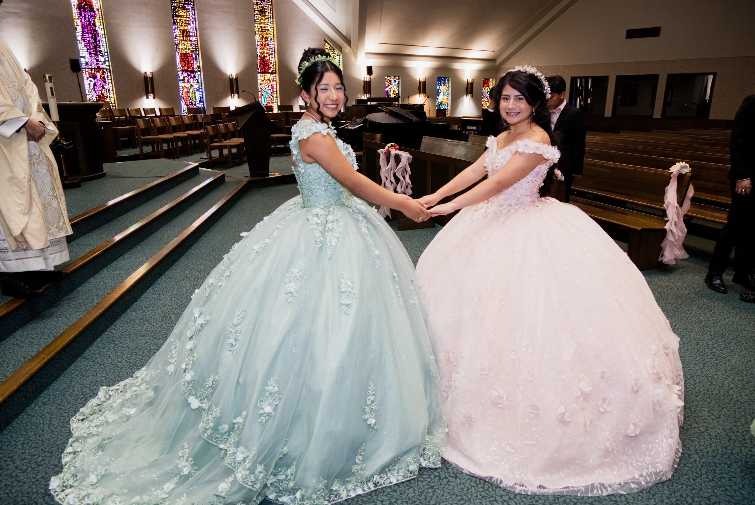 Two quinceañeras holding hands in green and pink gowns inside a church